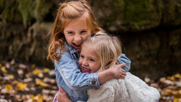 Two little girls smiling and hugging outside